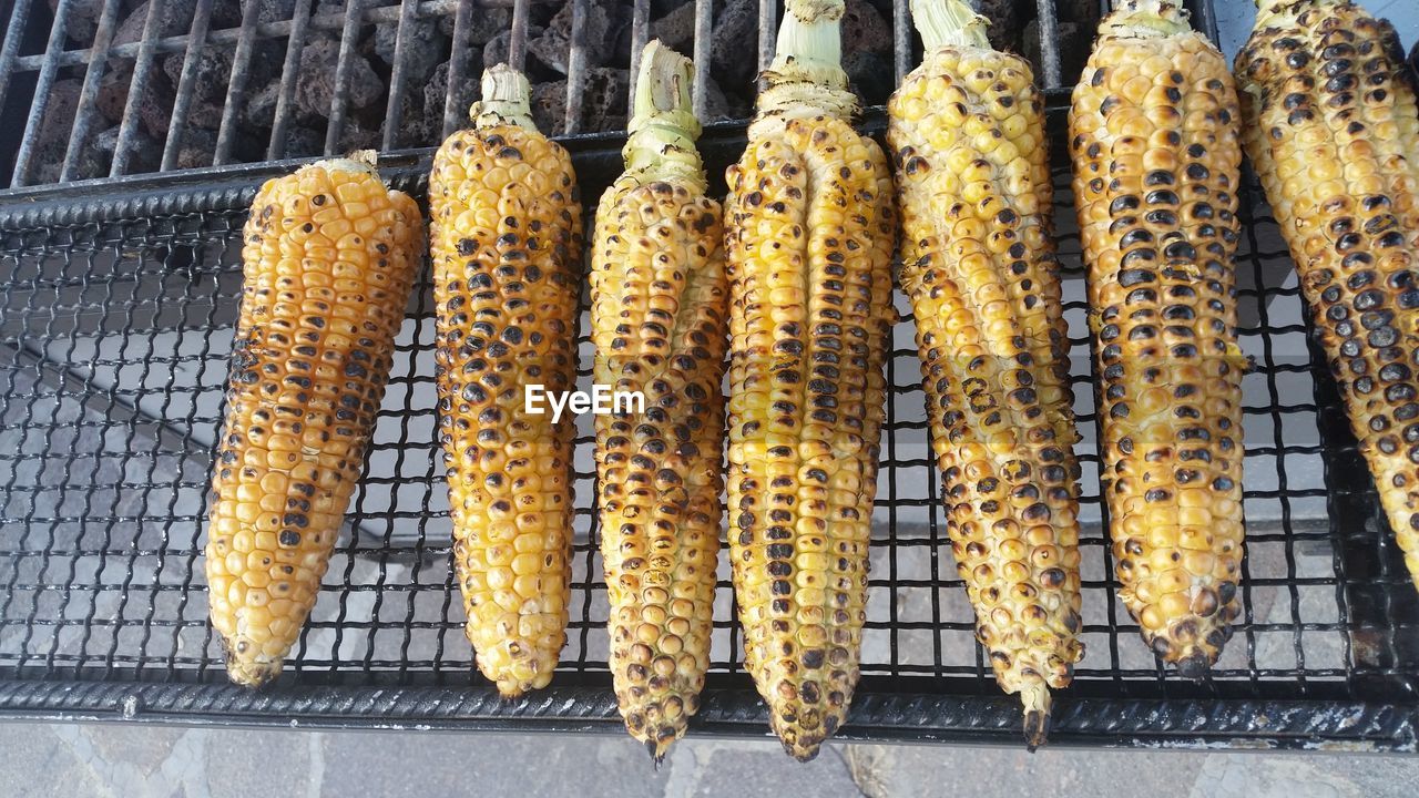 High angle view of roasted corns on metal grate over burning charcoal