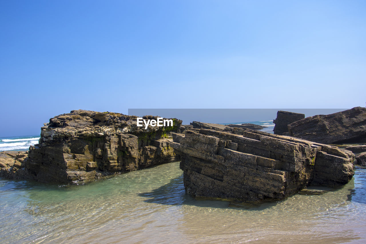 Rock formations by sea against clear blue sky