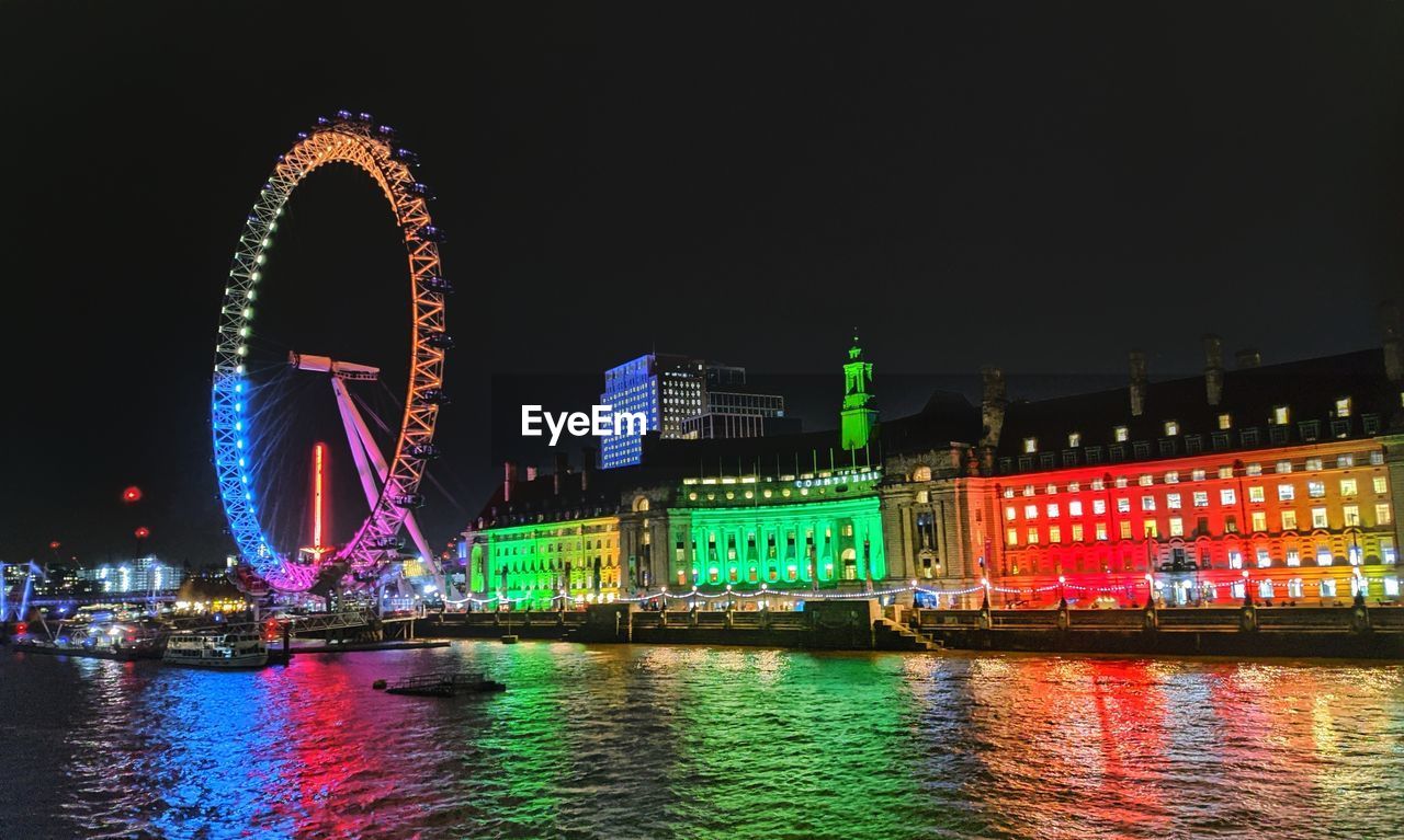 Illuminated ferris wheel by river at night