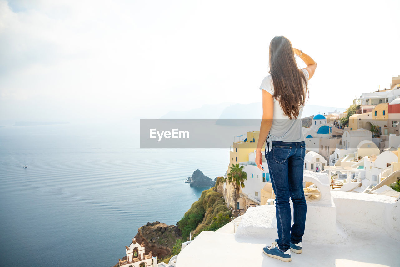 Full length of woman looking at view while standing in city by sea against sky