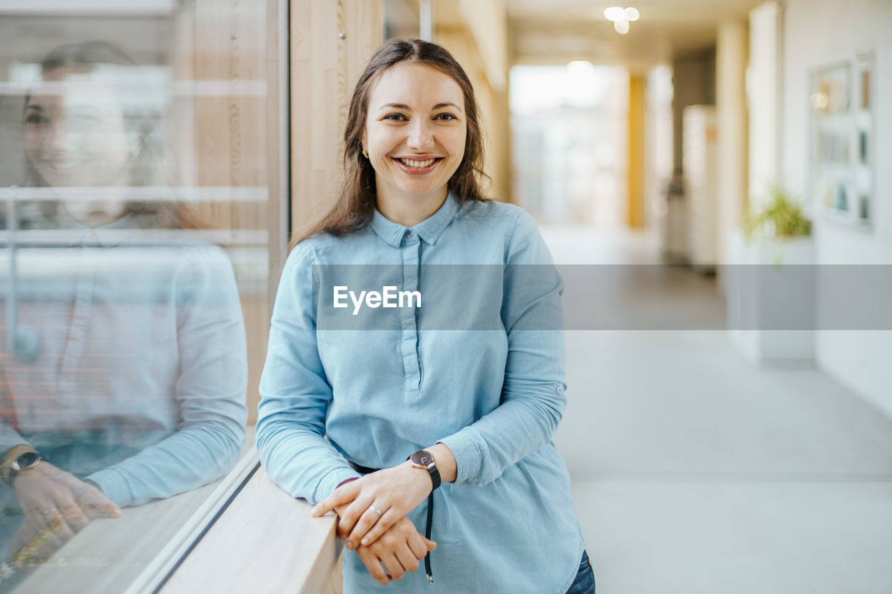 Portrait of happy young businesswoman standing at office corridor