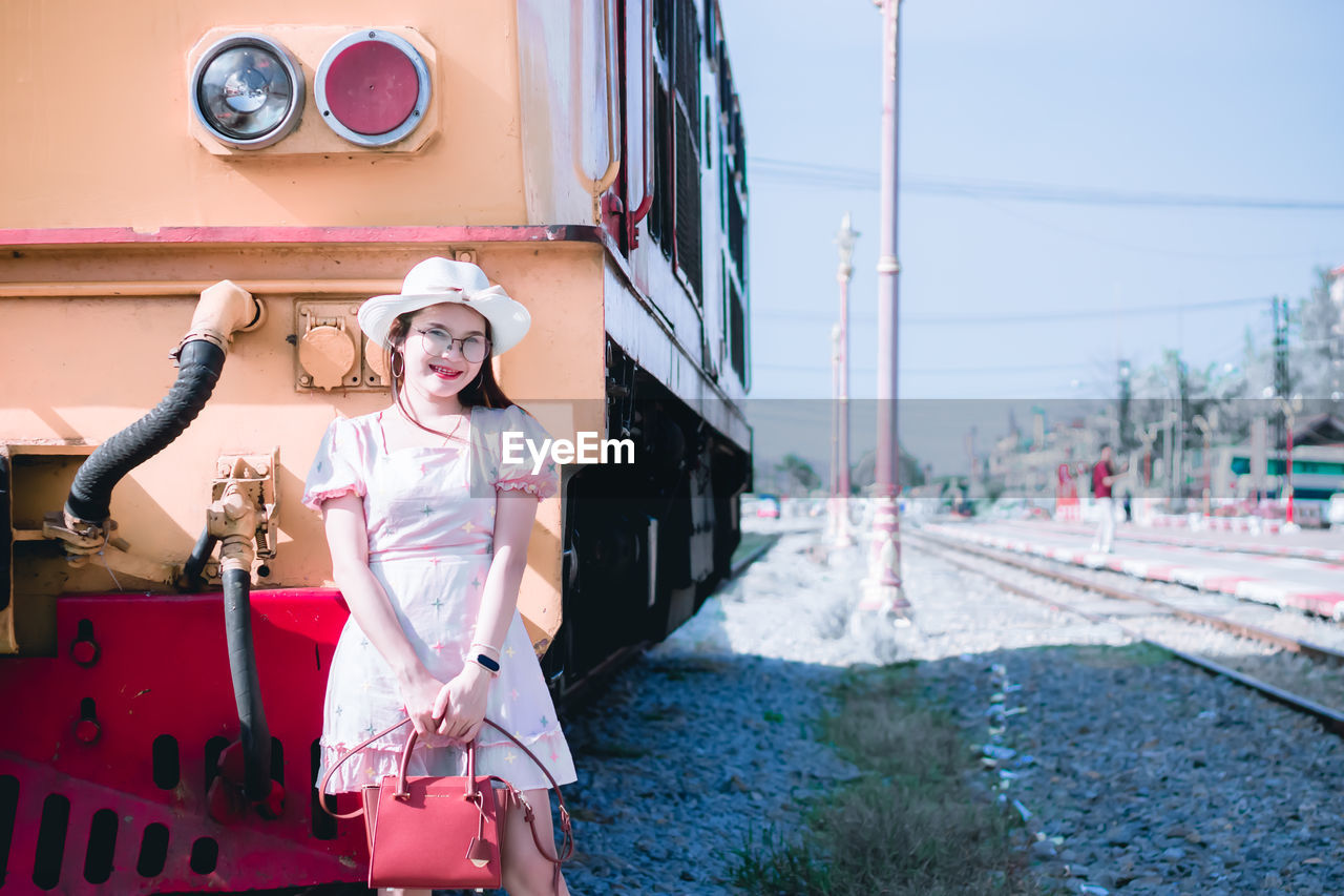 Portrait of smiling woman standing by locomotive by railroad track