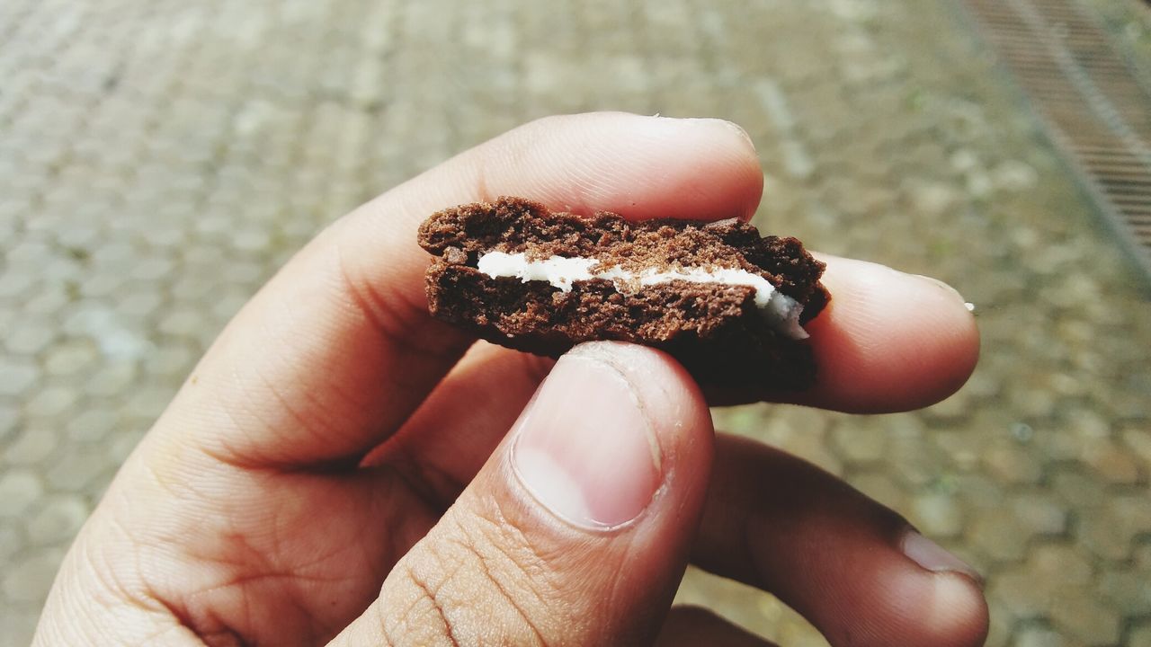 Cropped hand holding cookie over footpath