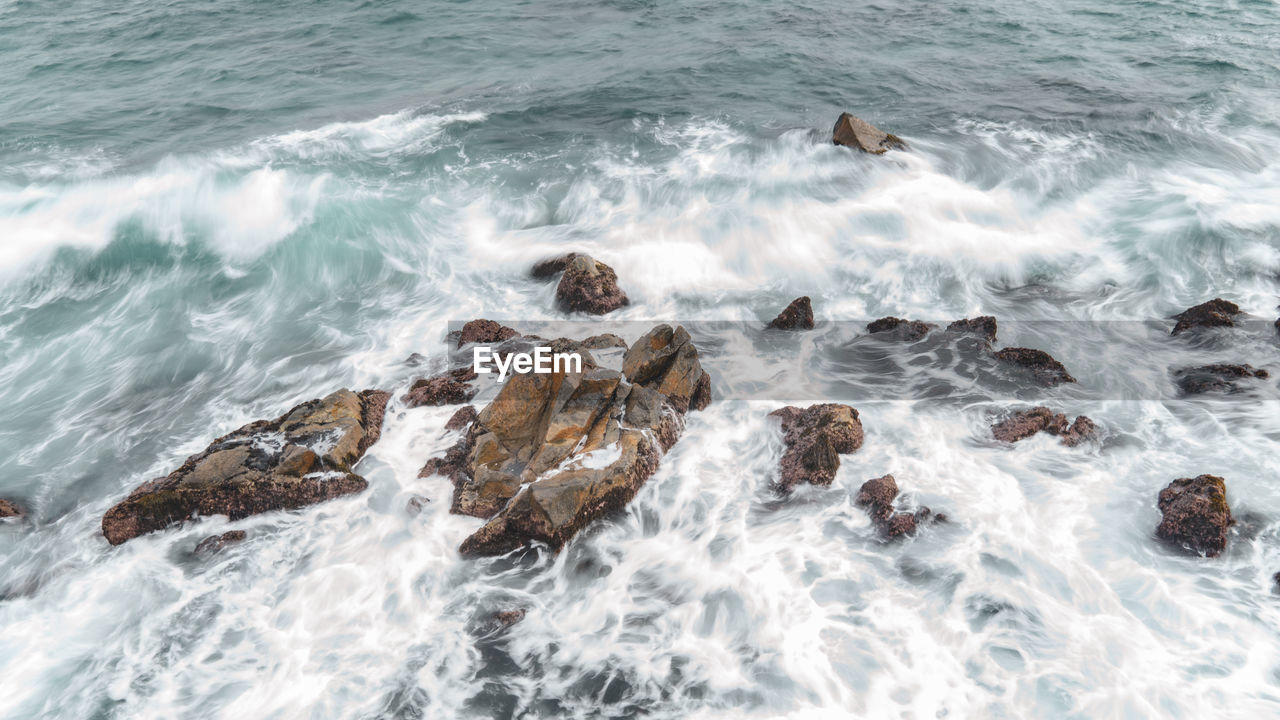 HIGH ANGLE VIEW OF WAVES SPLASHING ON ROCKS