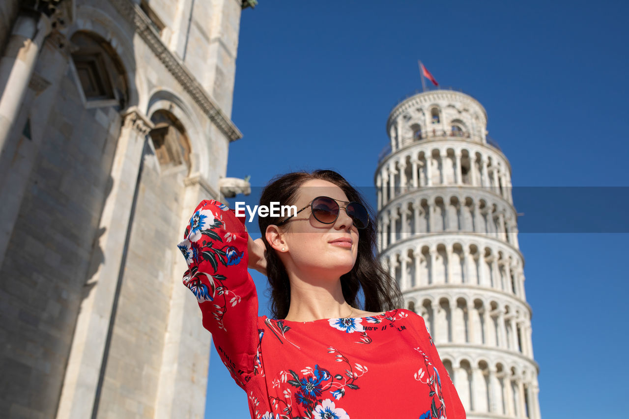 Woman with hand in hair standing against leaning tower of pisa in italy