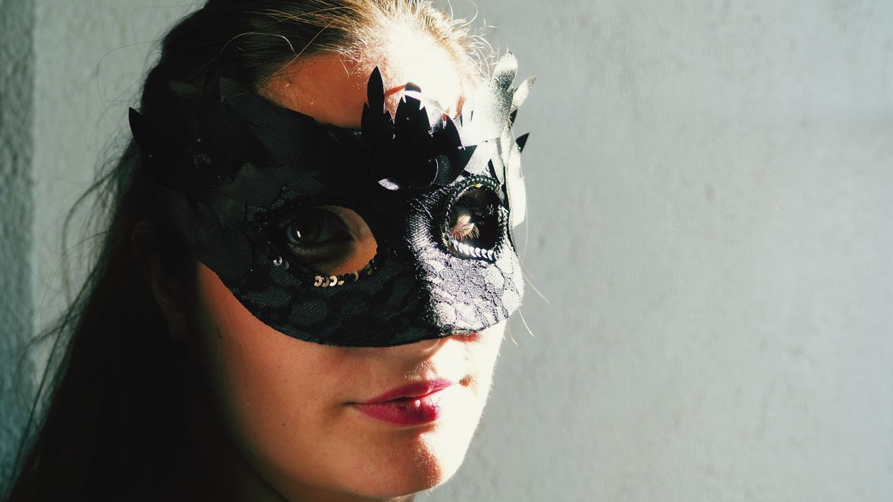 Close-up portrait of woman wearing eye mask against wall