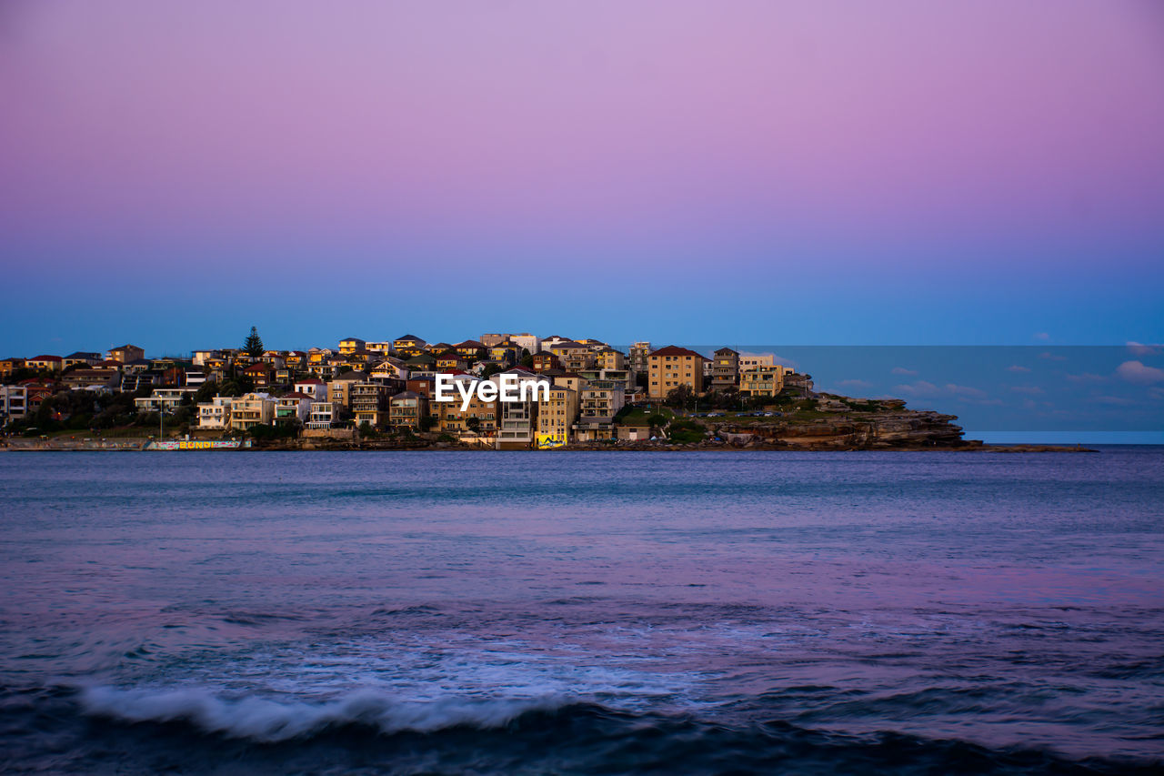 Scenic view of sea by buildings against sky during sunset