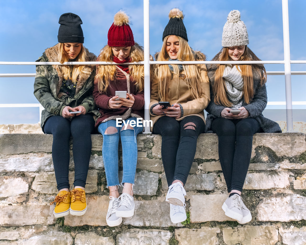 Four friends sitting side by side on a wall text messaging