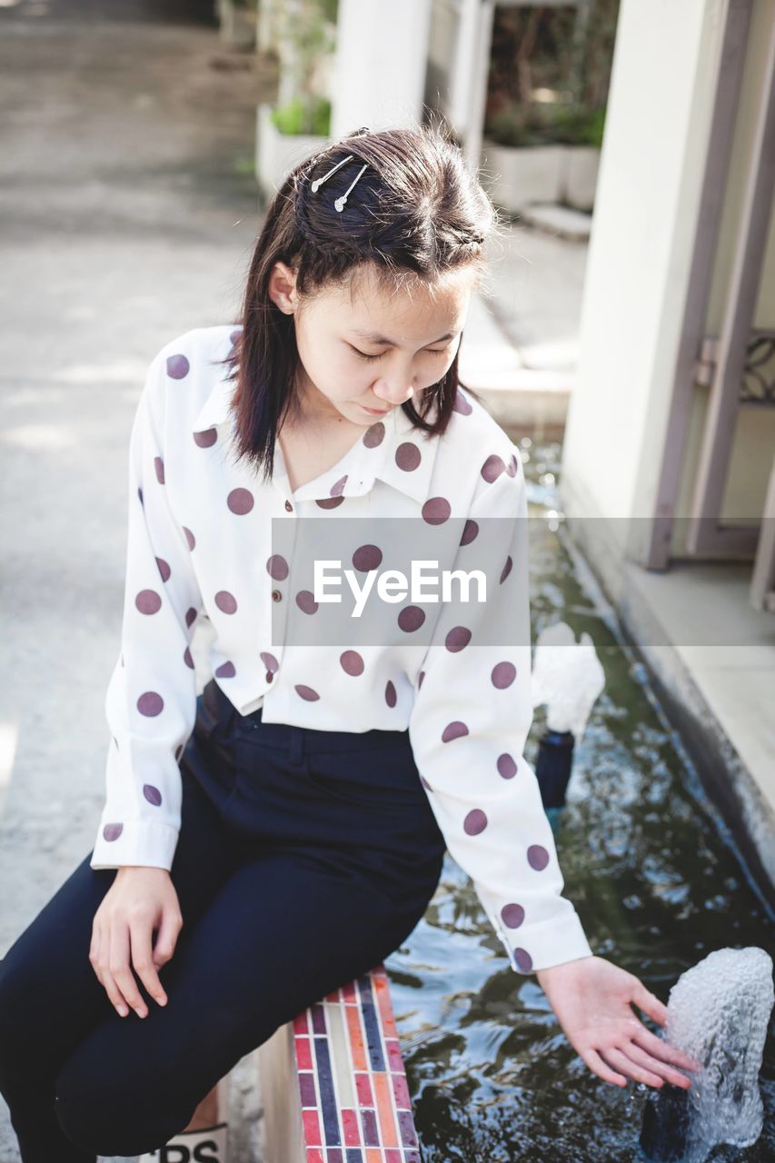 Girl sitting by water fountain outdoors