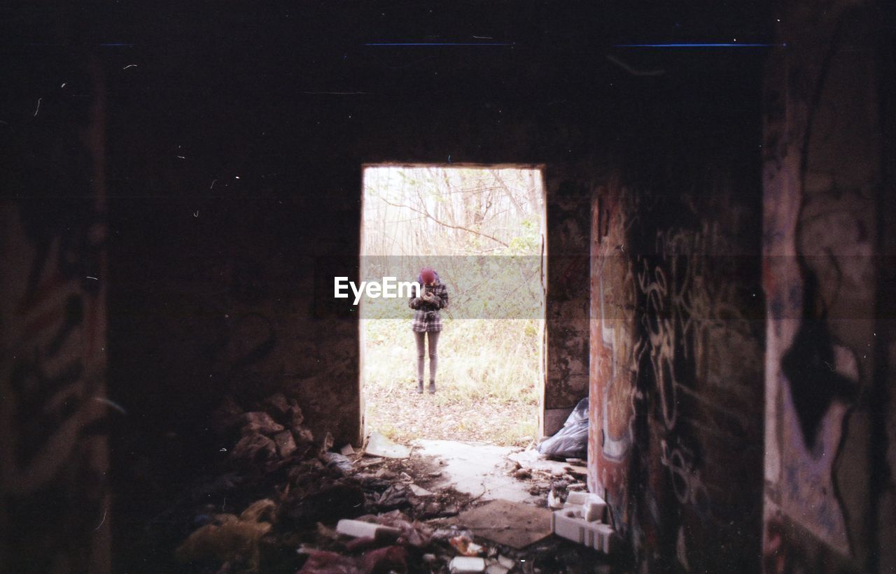 REAR VIEW OF WOMAN STANDING IN ABANDONED ENTRANCE