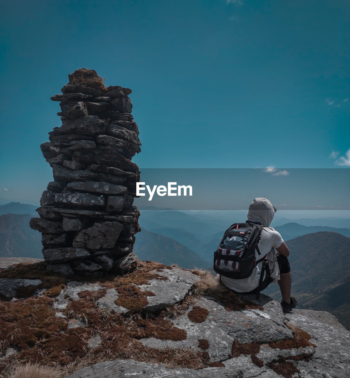 Man sitting on the top of the hill and looking to the mountains under the blue sky.