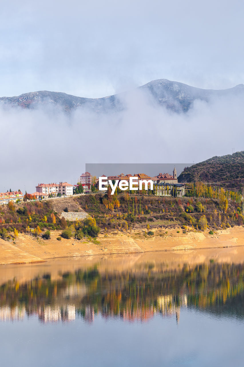 Typical residential buildings located on hill above calm river in scenic mountainous valley on sunny autumn day in riano