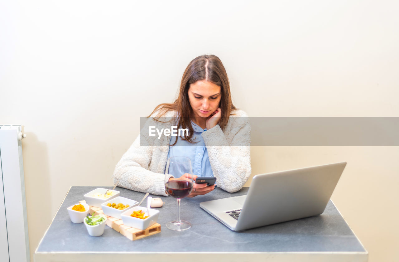 Young woman using mobile phone with food and laptop on table