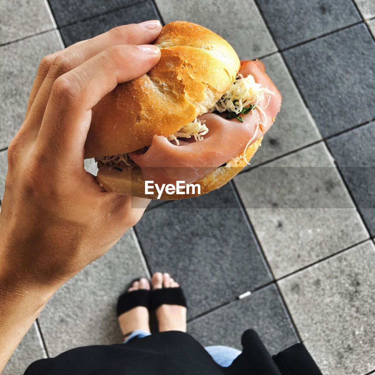 Low section of woman holding burger on footpath