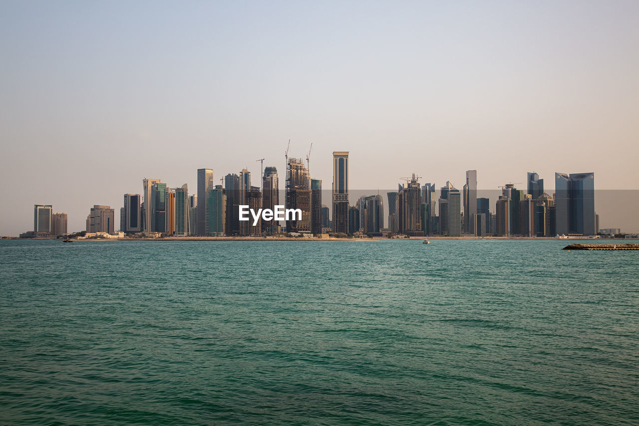 Sea by modern buildings against clear sky