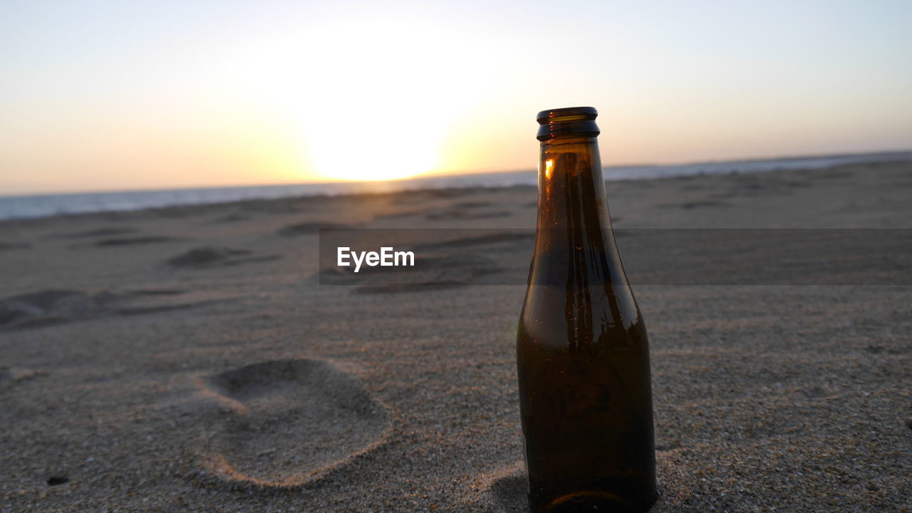 CLOSE-UP OF BEER GLASS BOTTLE ON BEACH