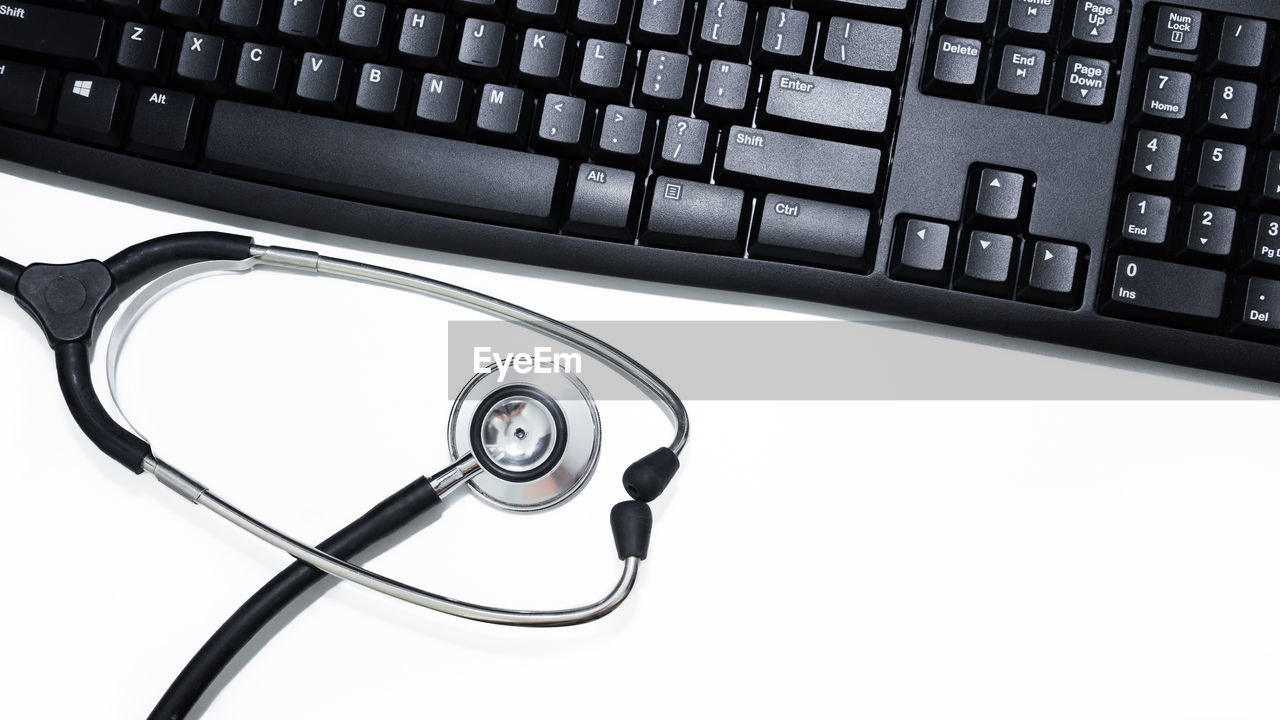 High angle view of laptop keyboard and stethoscope over white background
