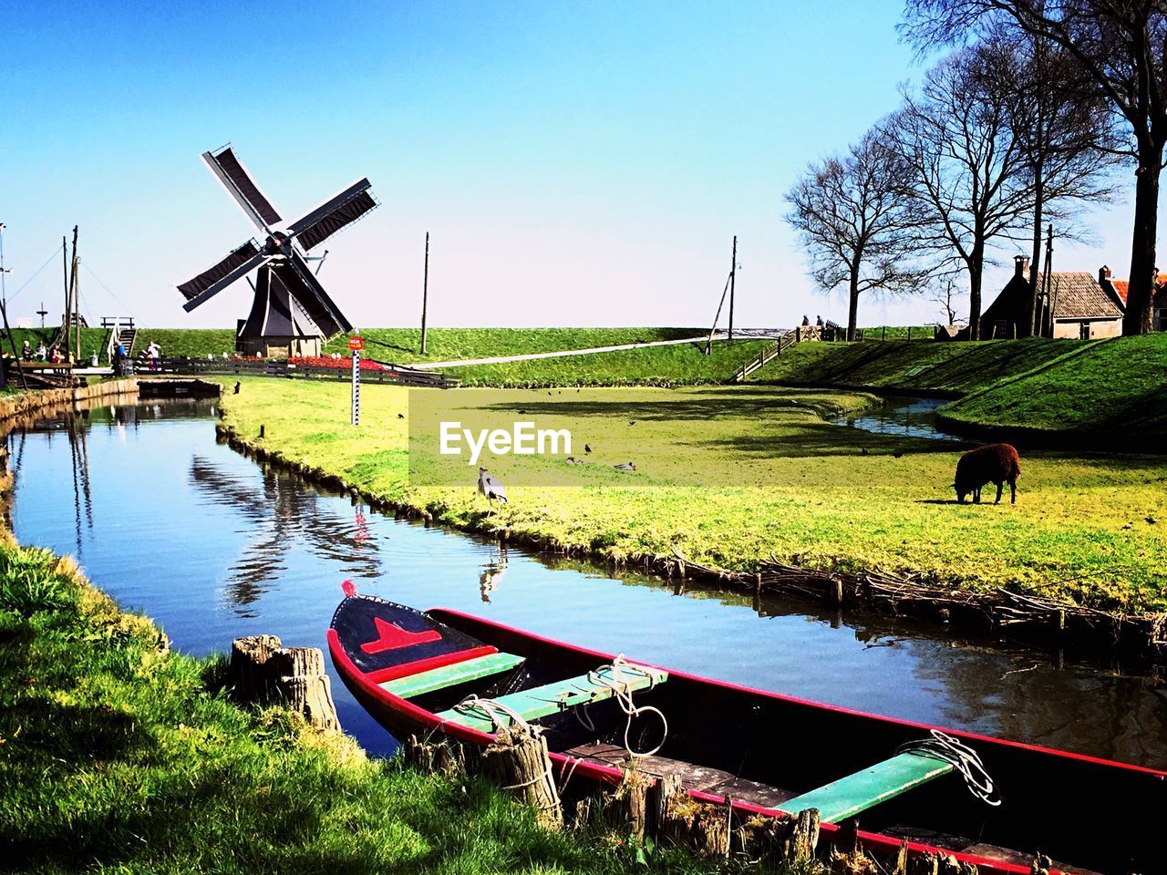 Boat moored in river amidst field in front of traditional windmill at zuiderzee museum