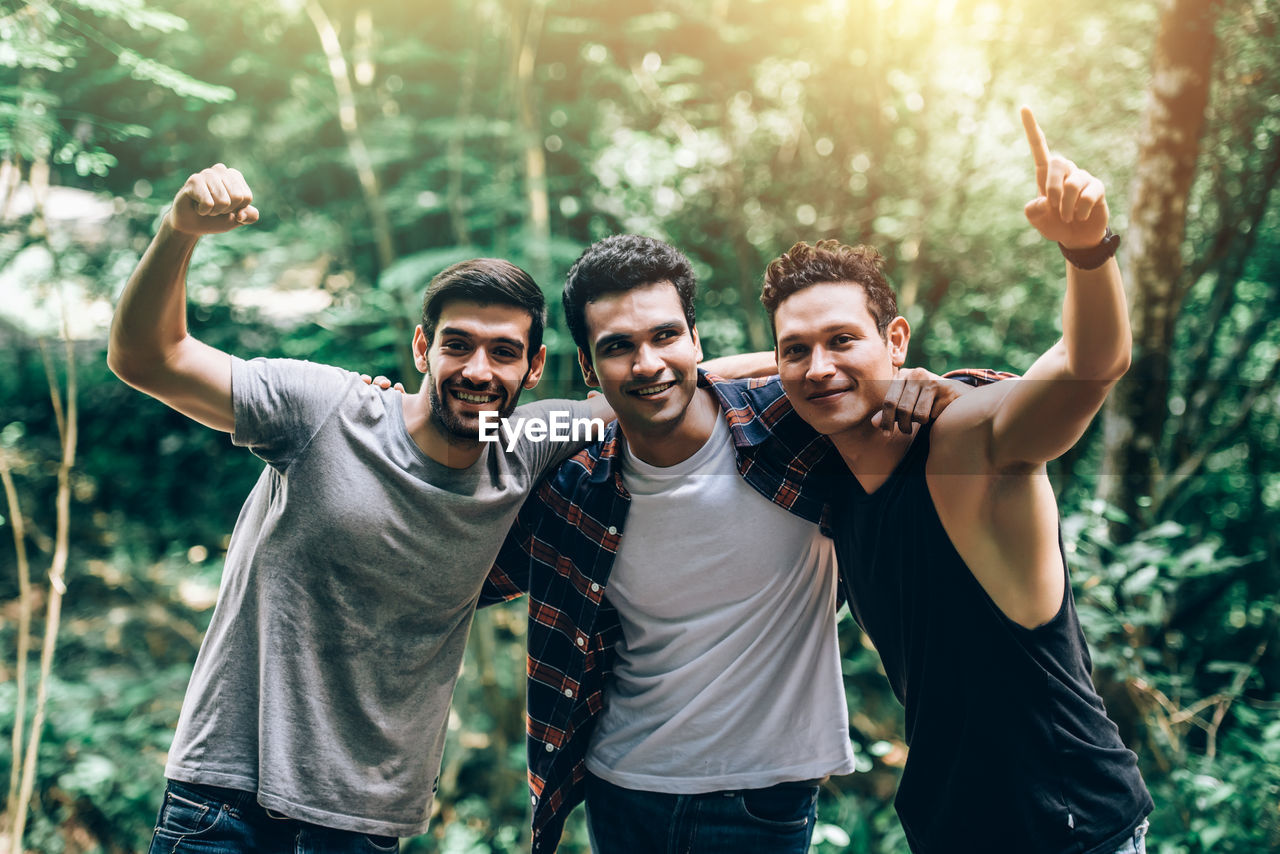 Smiling friends gesturing while standing in forest