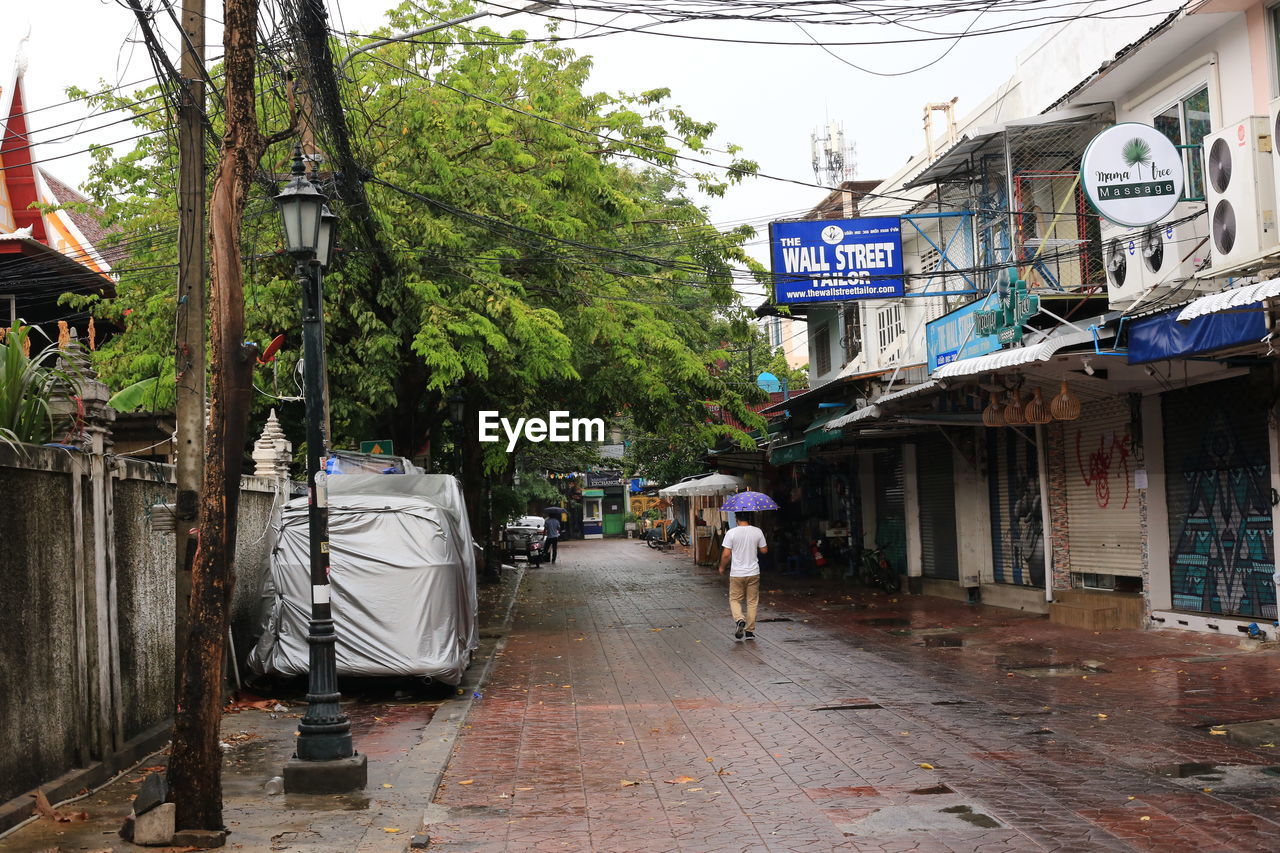 REAR VIEW OF PEOPLE WALKING ON WET STREET