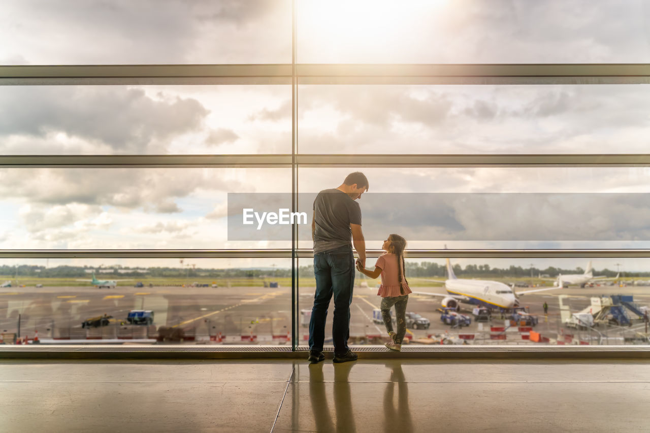 People at airport against sky seen through glass window