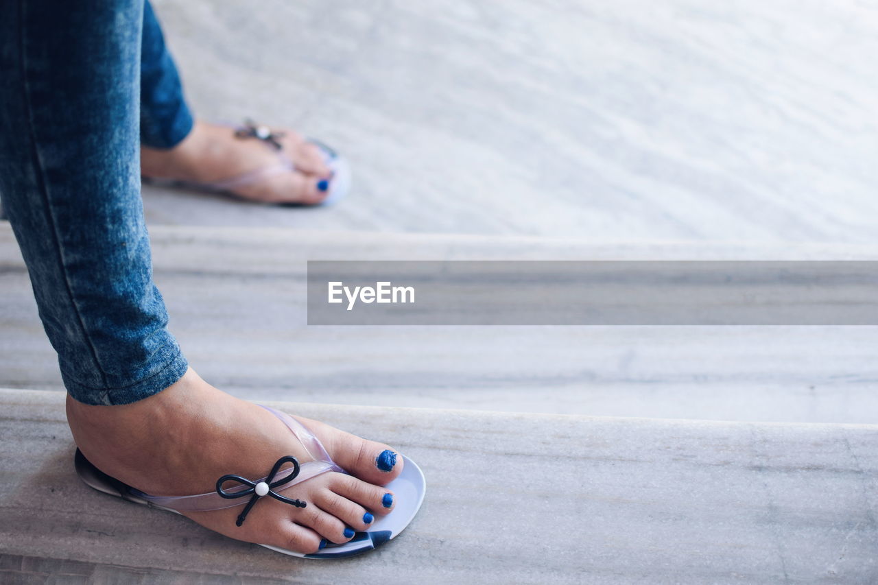 Low section of woman wearing flip-flops while standing on hardwood floor