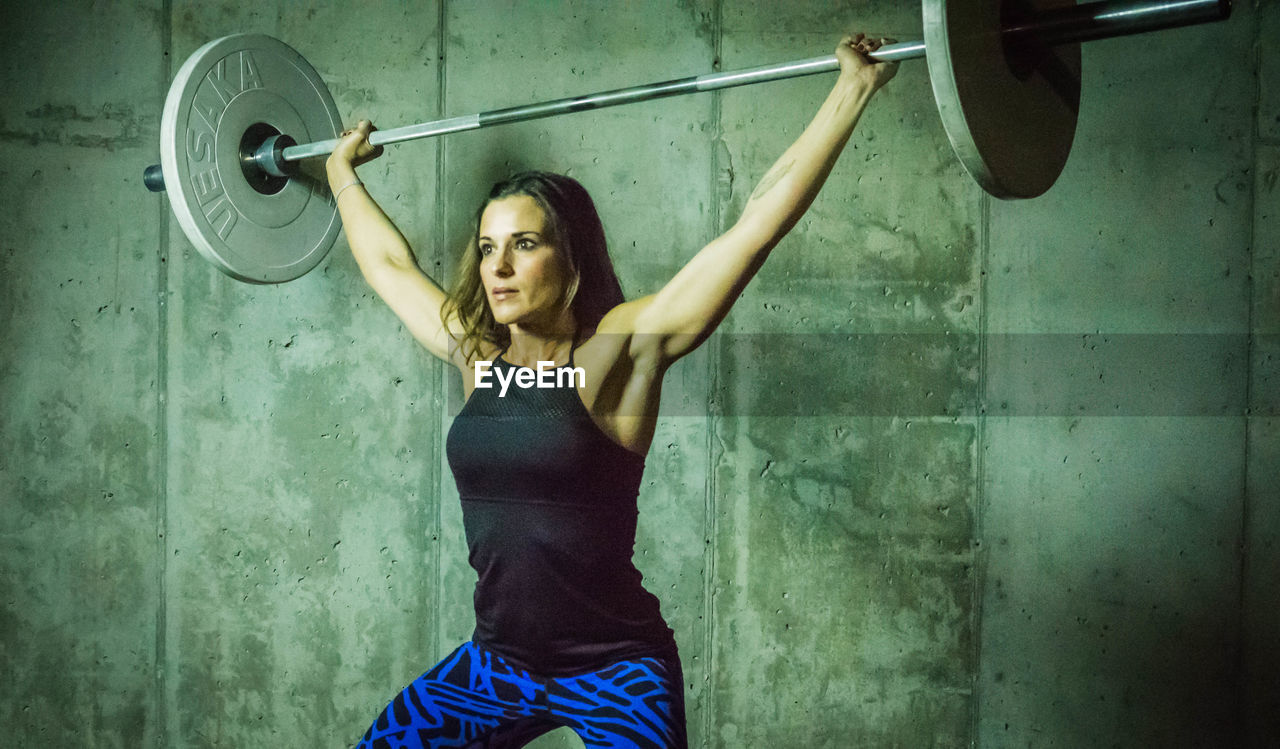 Beautiful woman lifting barbell against wall