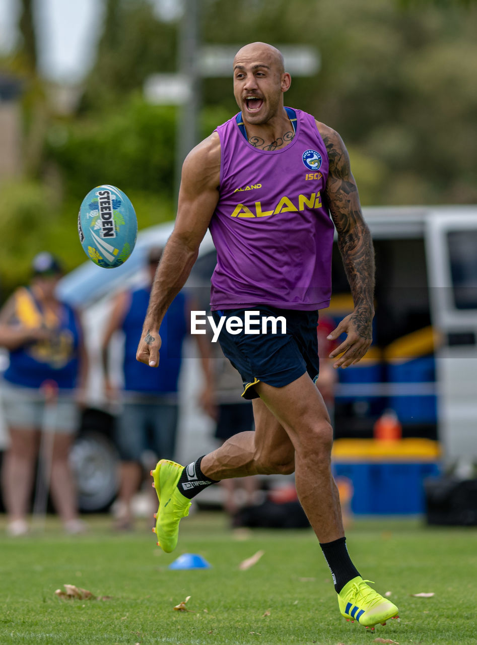 FULL LENGTH OF MAN RUNNING WITH BALL IN BACKGROUND