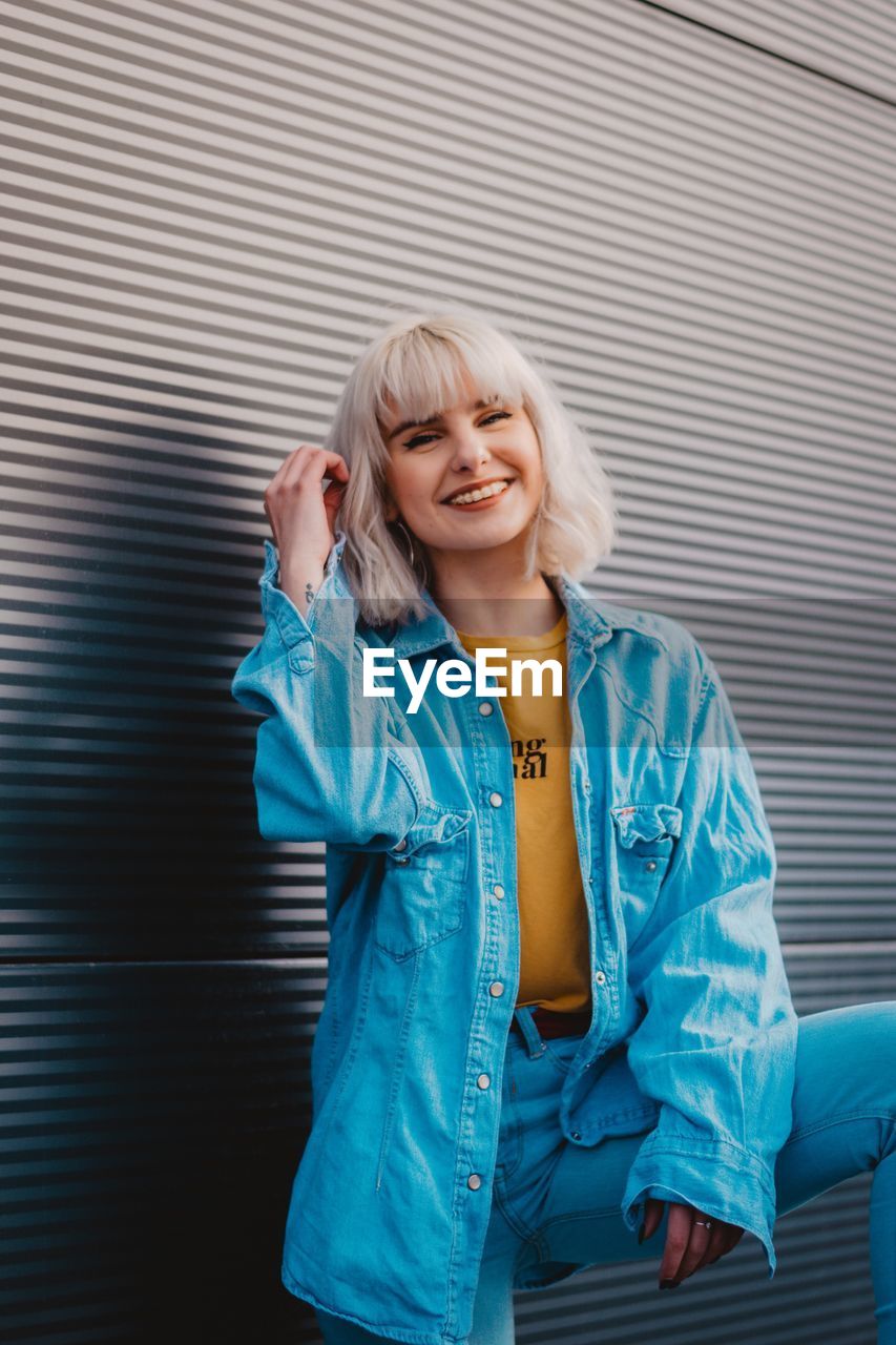 Portrait of happy young woman standing against wall