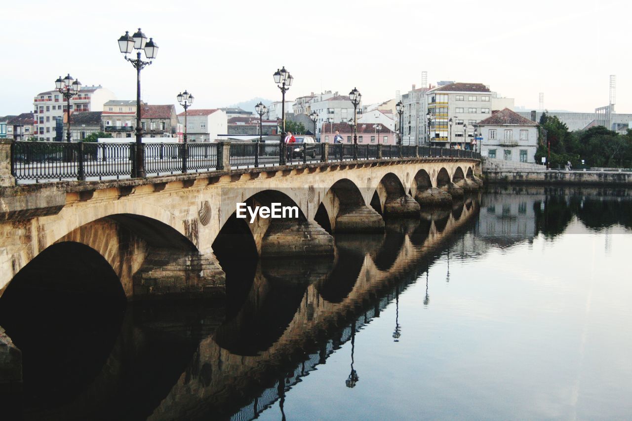 Arch bridge over river against sky in city