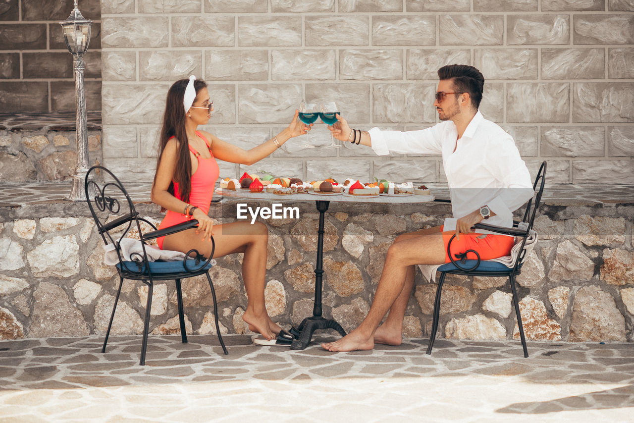 Young couple sitting by swimming pool and holding wine glasses