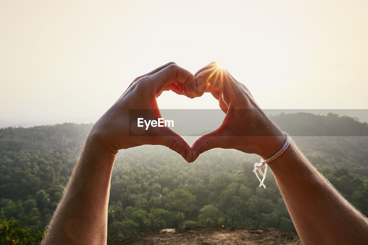 Close-up of hand making heart shape against sky
