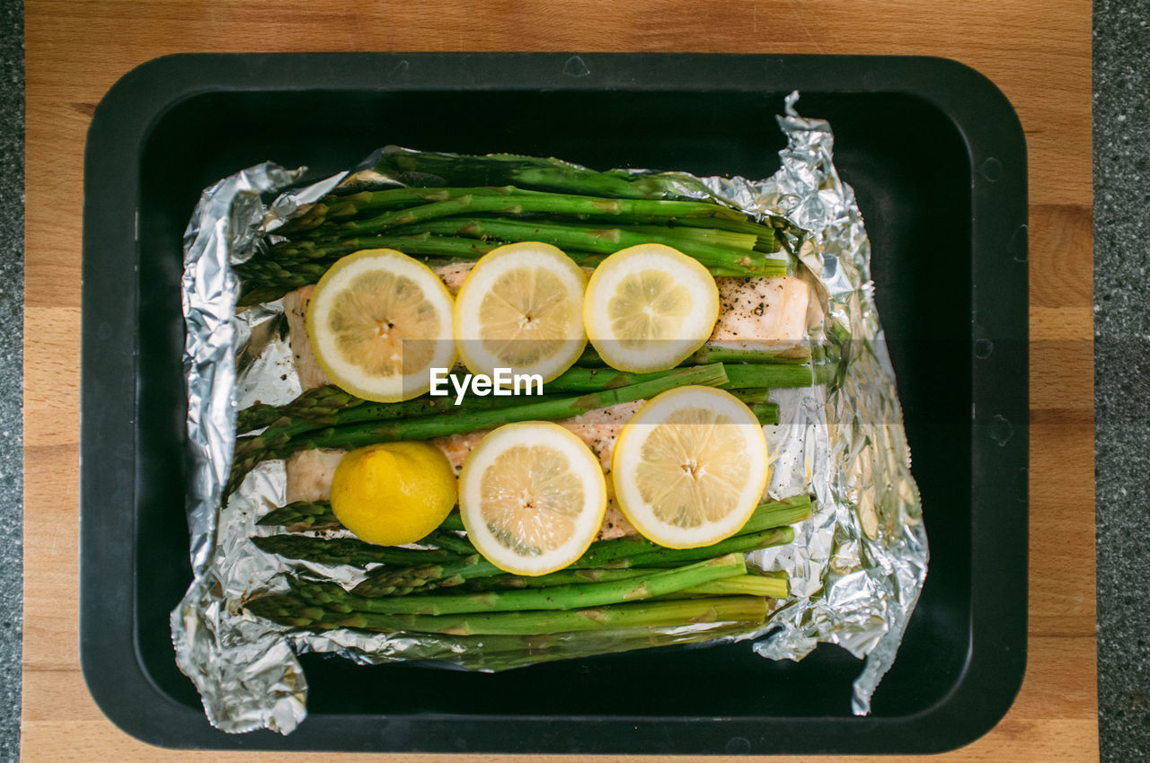 Directly above shot of lemon slices and asparagus with salmon in container