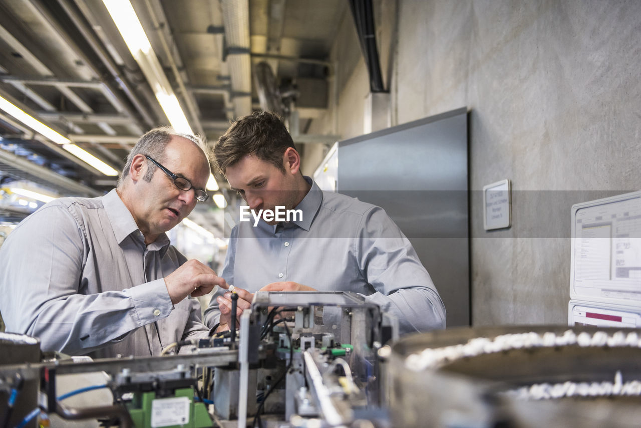 Two men in factory shop floor examining outcome of a machine