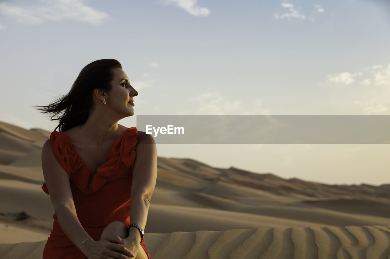 Woman looking away while sitting on land against sky