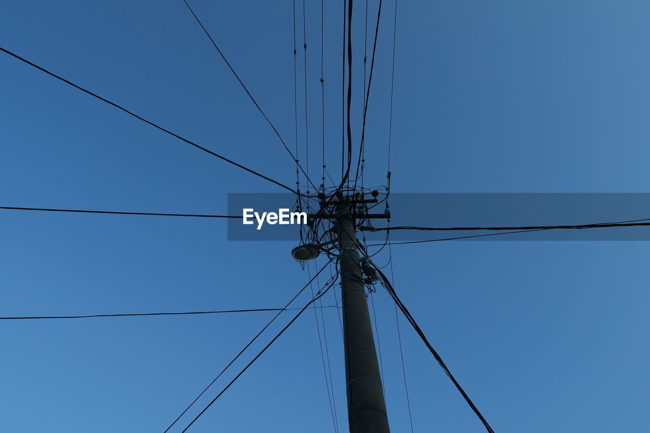 Low angle view of electricity pylon against blue sky