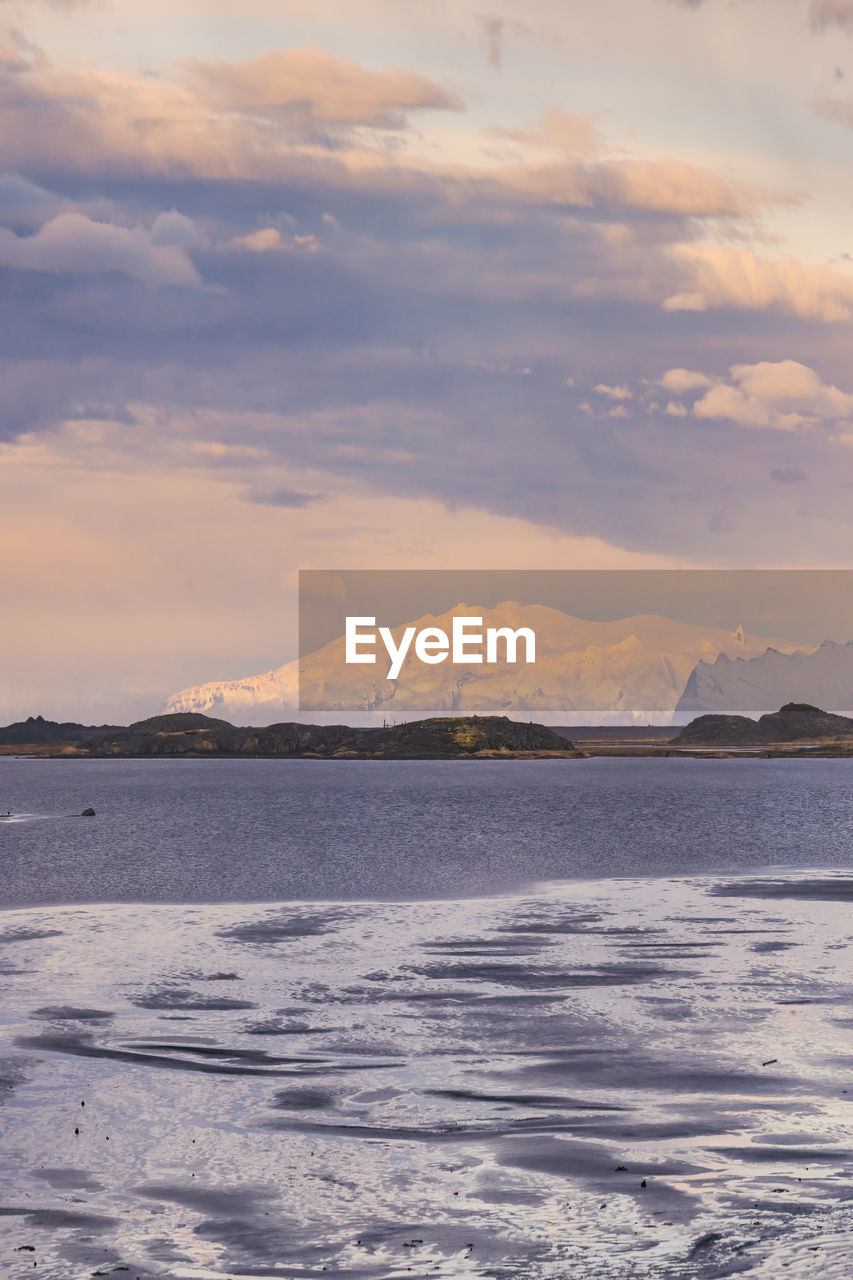 Scenic view of rocky mountains with snow in winter near stockness beach under cloudy sky in iceland