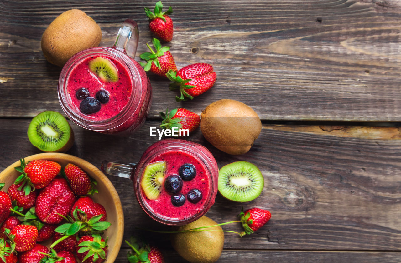 Smoothie with strawberries, kiwi and blueberries in jars on rustic wooden background.