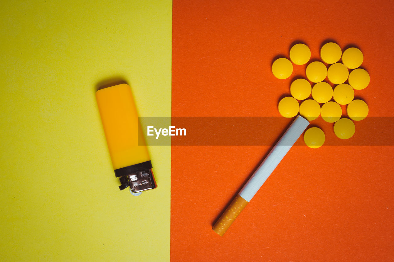 Directly above shot of cigarette with lighter and pills on colored background