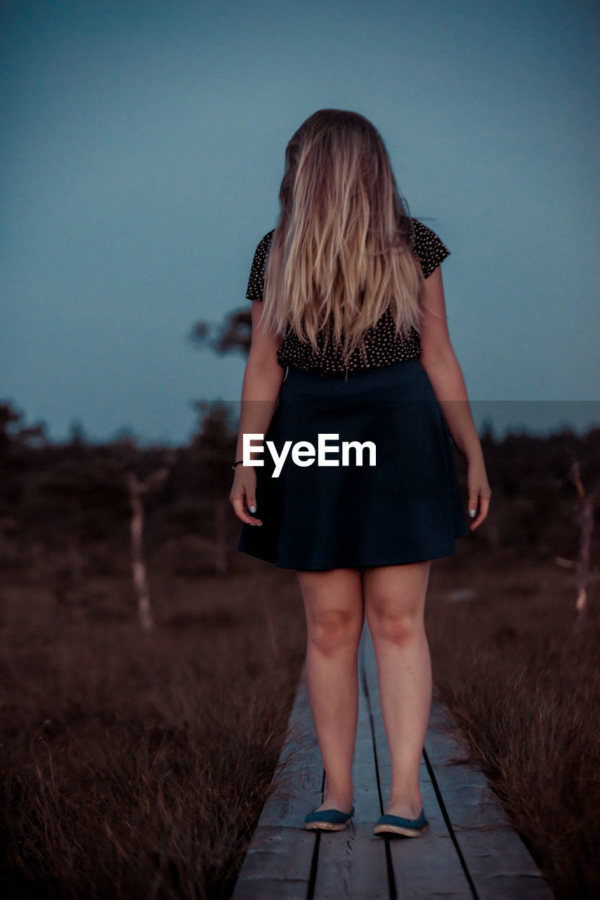 Teenage girl standing on boardwalk against clear sky