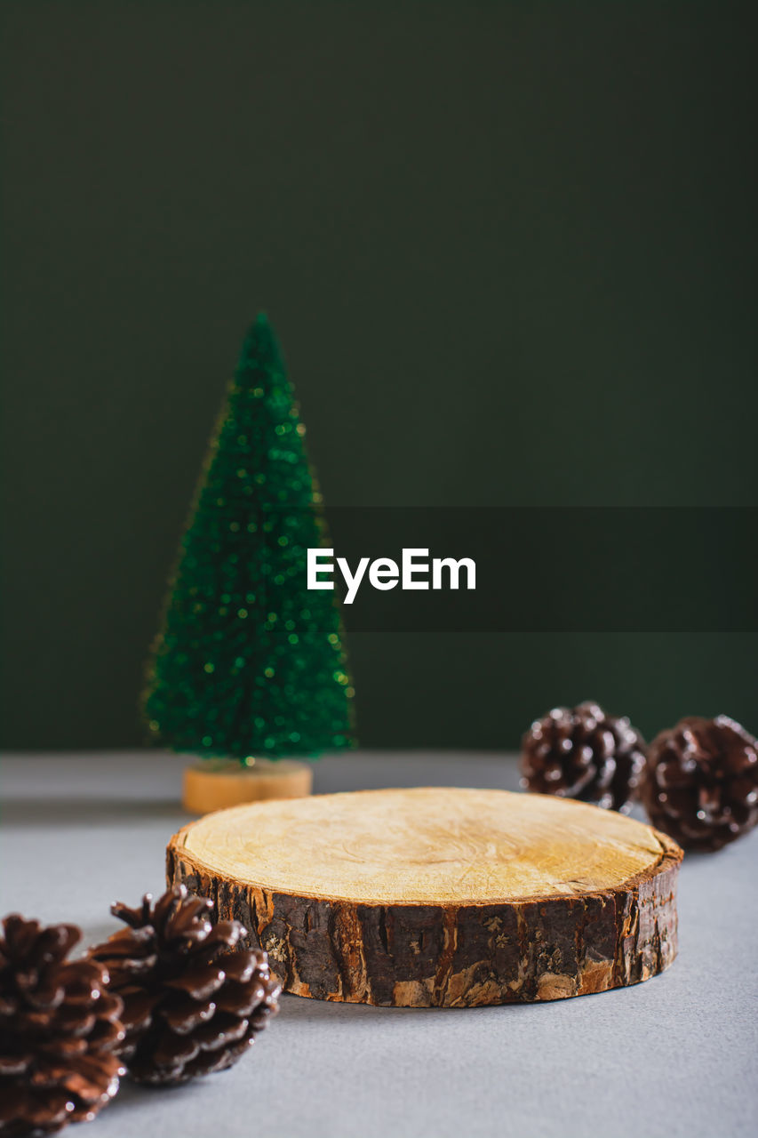 Podium made from a cut tree trunk, christmas tree and pine cones on a green vertical view