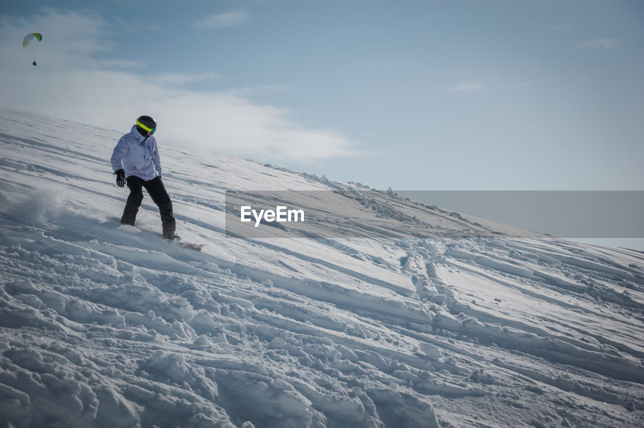 REAR VIEW OF MAN STANDING ON SNOWCAPPED MOUNTAIN AGAINST SKY