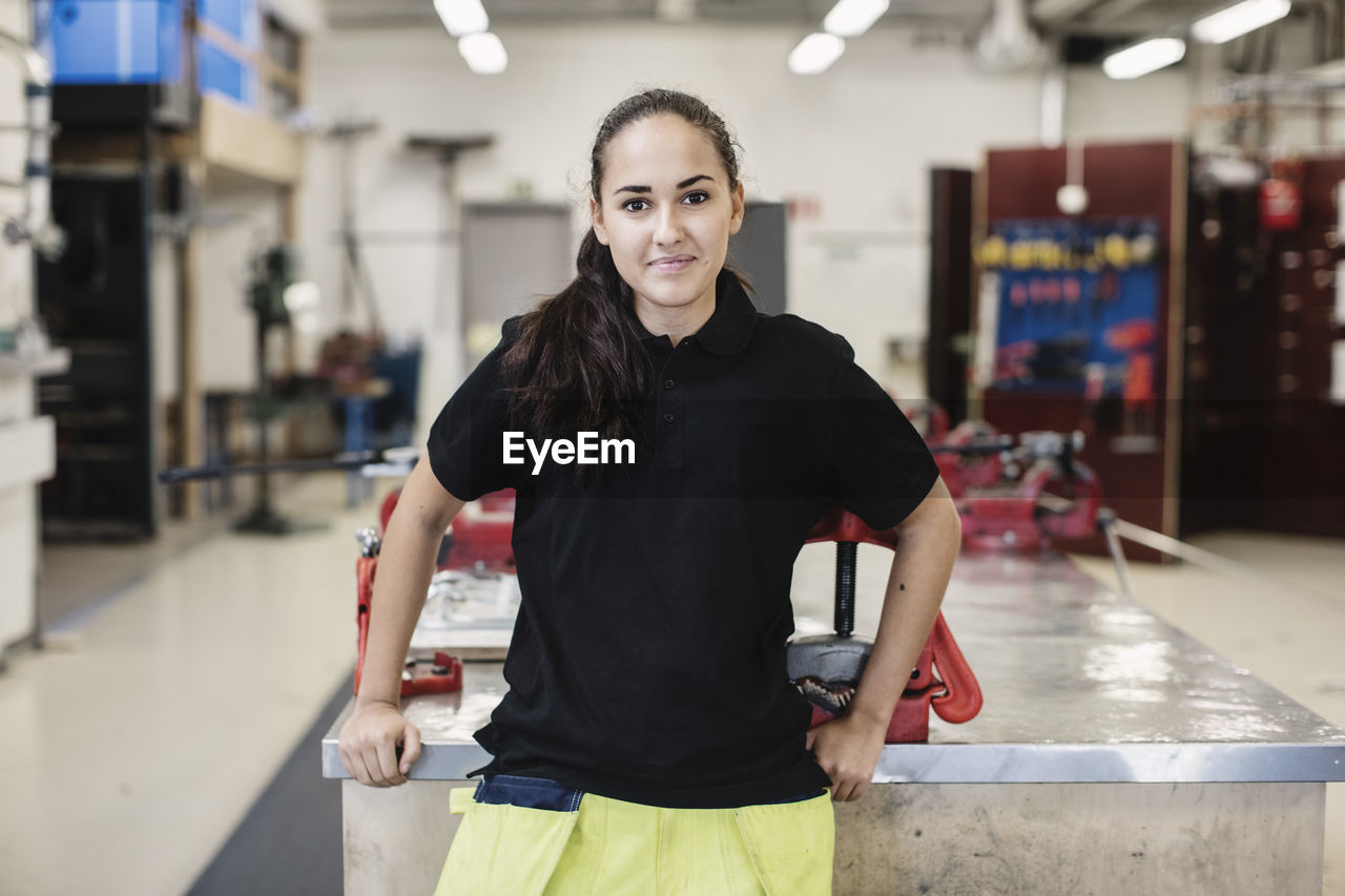 Portrait of smiling female auto mechanic student standing in workshop