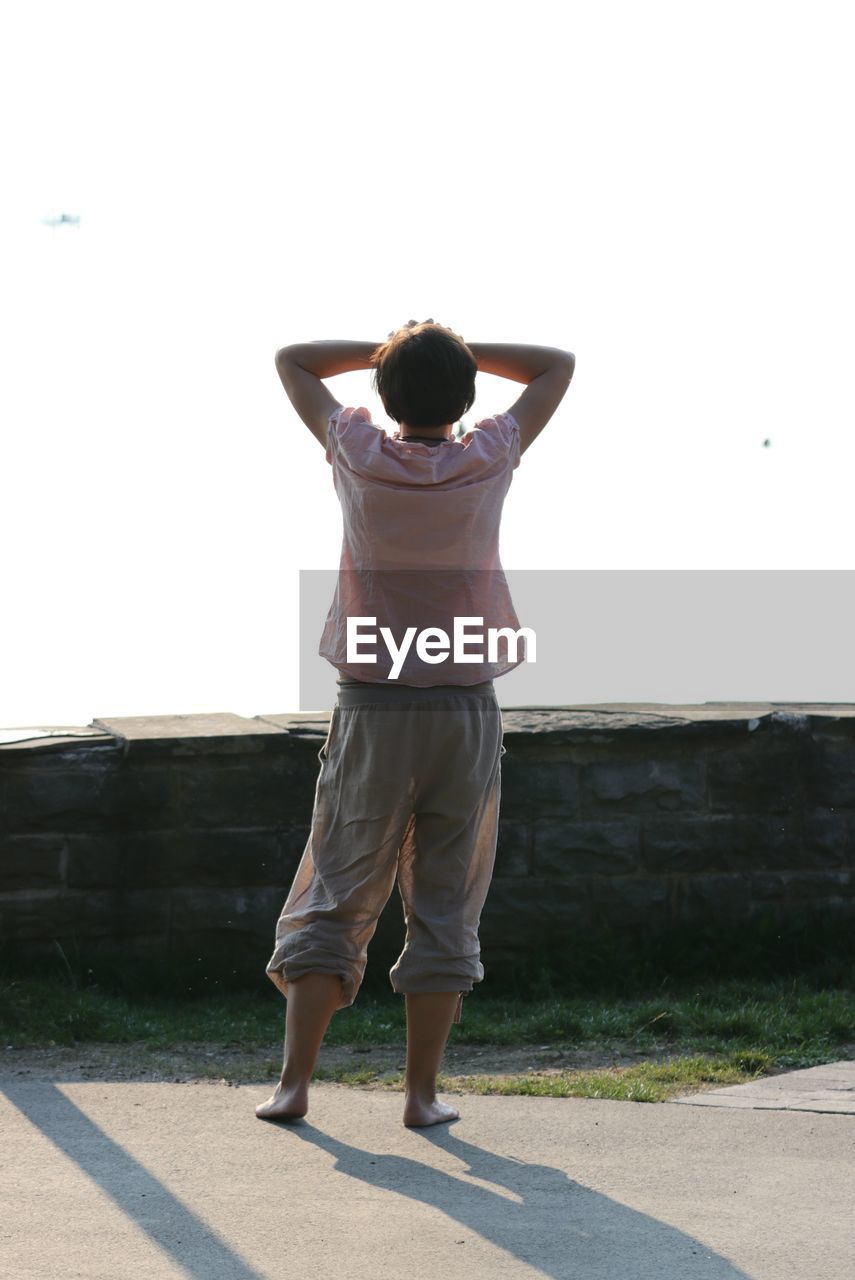 REAR VIEW OF WOMAN STANDING IN PARK AGAINST SKY