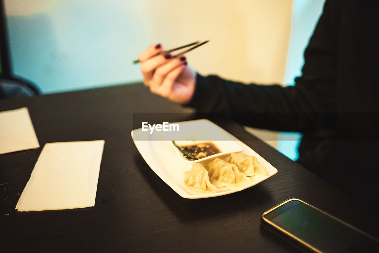 Midsection of woman holding chopsticks while having food at restaurant