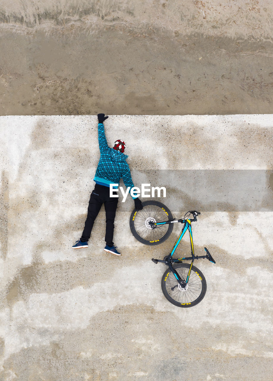 Rear view of man hanging from a concrete wall and holding a wheel