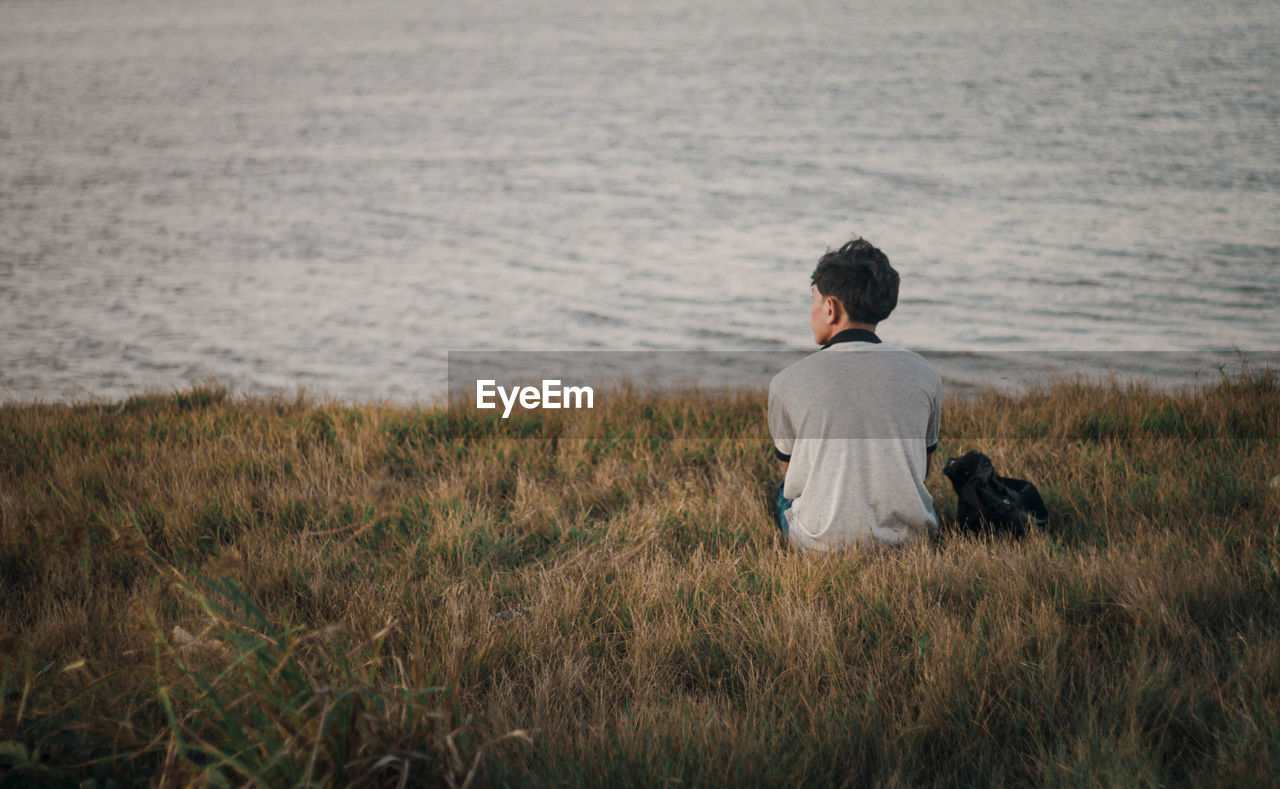 Rear view of man sitting by lake