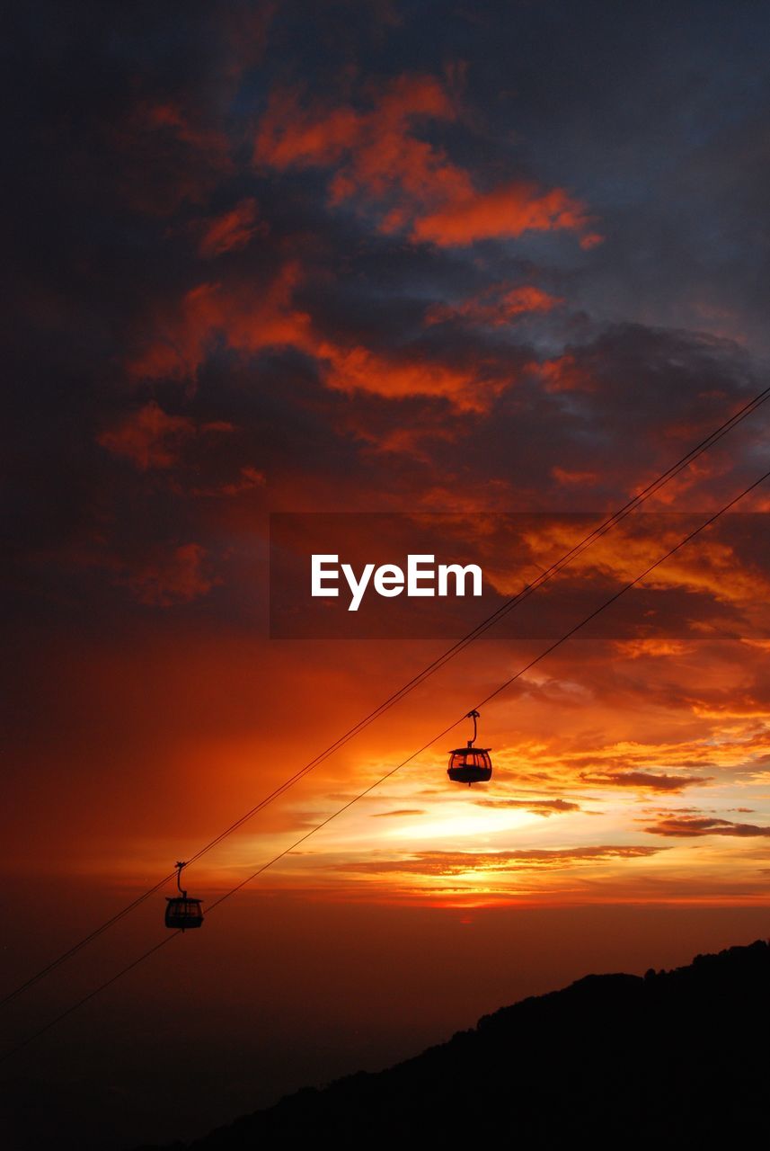 SILHOUETTE OF OVERHEAD CABLE CAR AGAINST ORANGE SKY