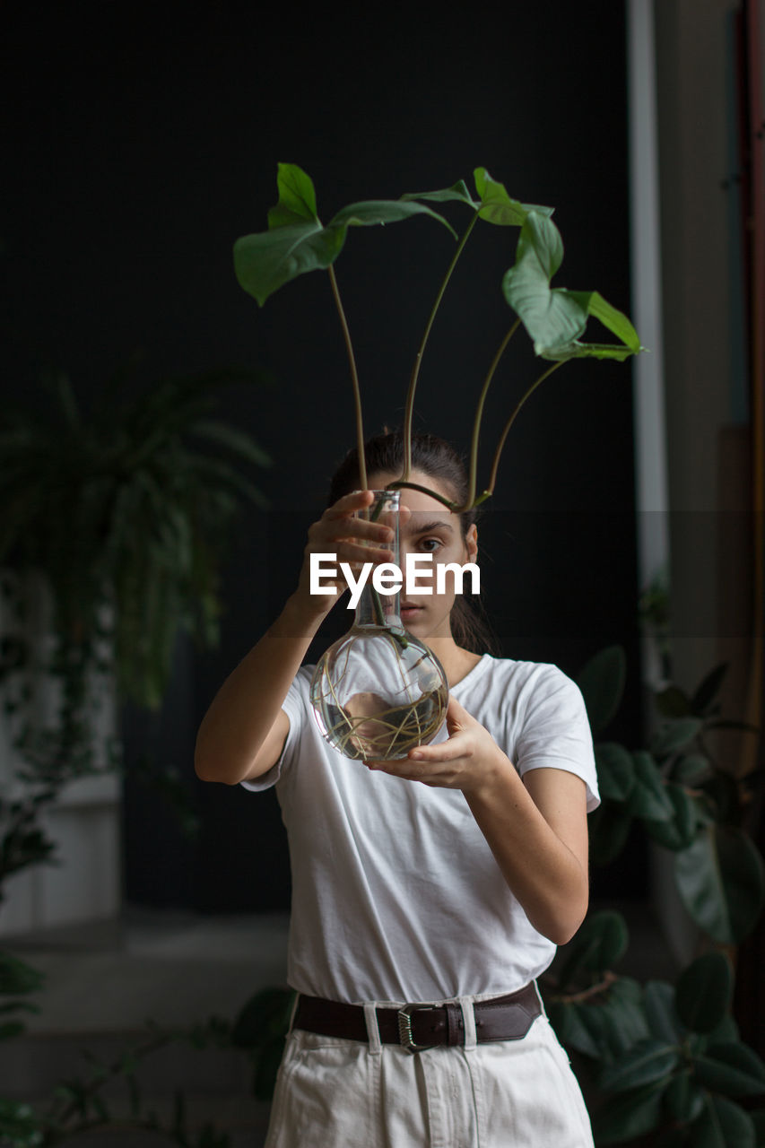 Woman gardener with natural makeup, holding a syngonium in glass flask in her green house