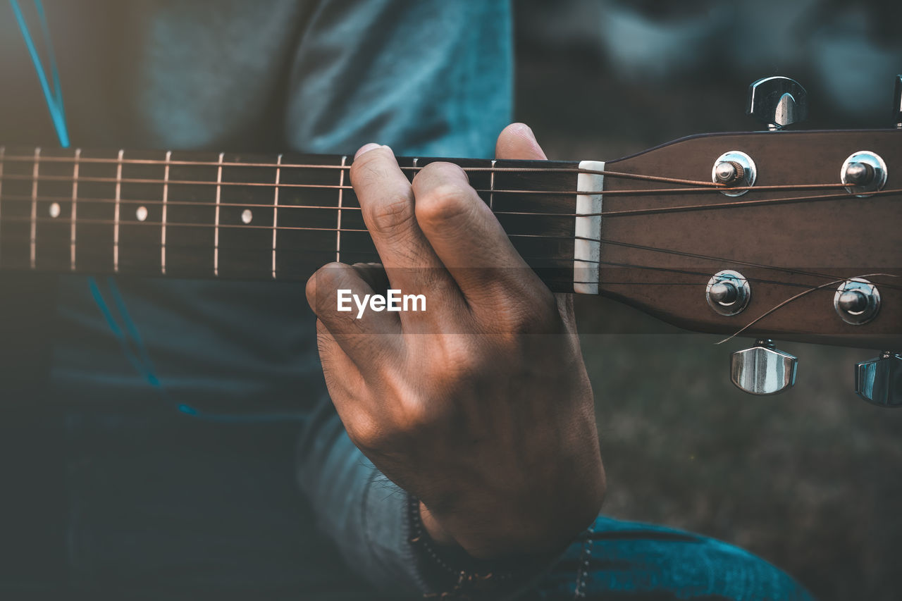 MIDSECTION OF MAN PLAYING GUITAR AT MUSIC CONCERT